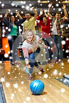 Happy young woman throwing ball in bowling club