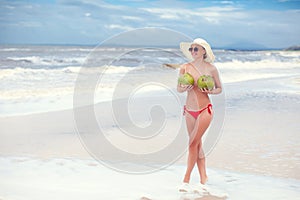 Happy young woman topless with coconuts in hands in straw hat with on the beach with a coconut