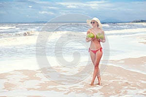 Happy young woman topless with coconuts in hands in straw hat with on the beach with a coconut