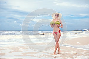 Happy young woman topless with coconuts in hands in straw hat with on the beach with a coconut