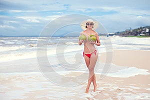 Happy young woman topless with coconuts in straw hat with on the beach with a coconut