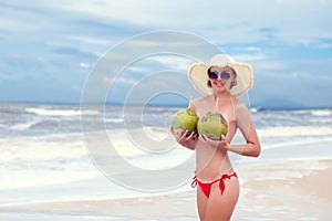 Happy young woman topless with coconuts in straw hat with on the beach with a coconut