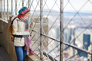 Happy young woman tourist at the observation deck of Empire State Building in New York City. Female traveler enjoying the view of