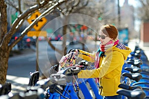 Happy young woman tourist ready to ride a rental bicycle in New York City at sunny spring day. Female traveler enjoying her time i
