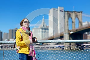 Happy young woman tourist sightseeing by Brooklyn Bridge, New York City, at sunny spring day. Female traveler enjoying view of dow