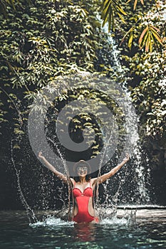 Happy Young woman tourist with straw hat in the deep jungle with waterfall. Real adventure concept. Bali island.