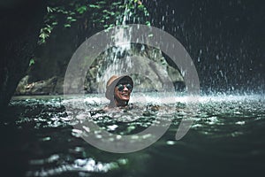 Happy young woman tourist swimming in the deep jungle with waterfall. Real adventure concept. Bali island.