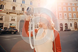 Happy young woman traveler photographer holds camera on European street and takes picture. Summer sun light