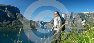 Happy young woman travels with a backpack in Norway, stands on a mountain with a beautiful landscape view from the Norwegian