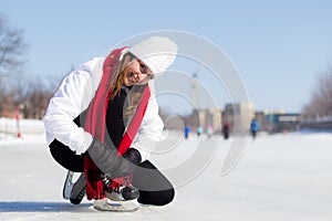 Happy young woman tying her ice skates in winter