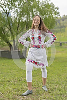 Happy young woman in the Ukrainian national clothes in the park. Woman in embroidery. Vertical photo