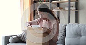 Happy young woman unpacking delivery parcel box at home