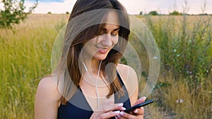 Happy young woman use smartphone and headphone standing in field at sunset, healthy lifestyle. Sportywoman runner using