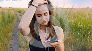 Happy young woman use smartphone and headphone standing in field at sunset, healthy lifestyle. Sportywoman runner using