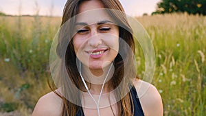 Happy young woman use smartphone and headphone standing in field at sunset, healthy lifestyle. Sportywoman runner using