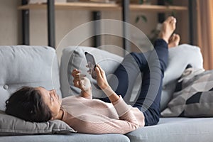 Happy young woman using cellphone, relaxing on sofa.
