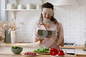 Happy young woman using digital computer tablet, cooking at home.