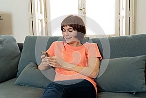 Happy young woman using her smart phone sitting on sofa at home. In leisure and spare time concept