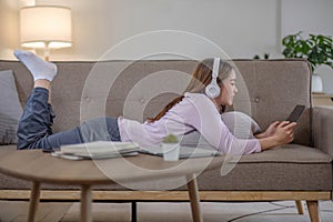 Happy young woman using laptop at home sitting on soft couch. Lady is working on laptop computer. Girl student is typing