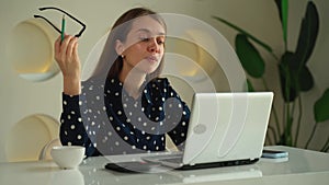 Happy young woman using a laptop, sitting at a desk, writing notes while watching a webinar, studying online, looking at