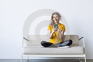 Happy young woman using mobile phone while sitting a couch at home with laptop computer