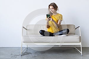 Happy young woman using mobile phone while sitting a couch at home with laptop computer