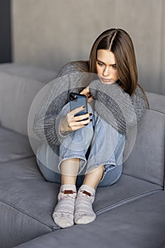 Happy young woman using mobile phone while sitting a couch at home with laptop computer