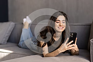 Happy young woman using mobile phone while sitting a couch at home with laptop computer