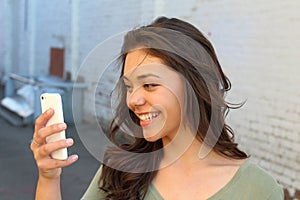 Happy young woman using a smart phone in the street with an unfocused background taking a selfie or using Skype or making a video photo