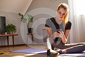Happy young woman using smart phone whilst working out at home