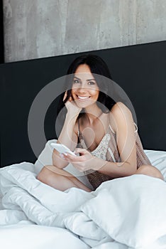 Happy young woman using smartphone in bed on self isolation