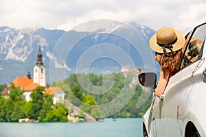 Happy young woman on vacation leaning out of car window on shore of Bled lake, country of Slovenia. Travel, holiday