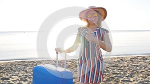 Happy young woman on vacation with a suitcase showing thumbs up