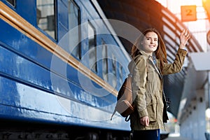 Happy young woman waitng train on the railway station platform. Woman travel with the train.