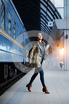 Happy young woman waitng train on the railway station platform. Woman travel with the train.