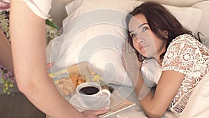 Happy young woman waking up when her husband brings her coffee in bed