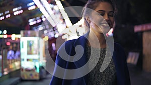 Happy young woman walking in amusement park, smiling and laughing. Different attractions on the background. Slowmotion