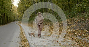 Happy young woman walking with dog along road in autumn park