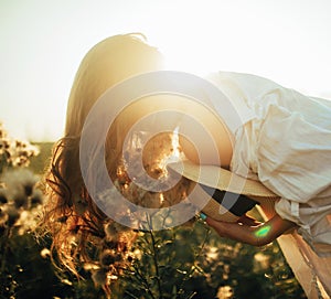 Happy young woman is walking among the flowers and grass on meadow at sunset