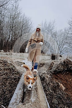 Happy young woman walking with her welsh corgi pembroke puppy, winter nature