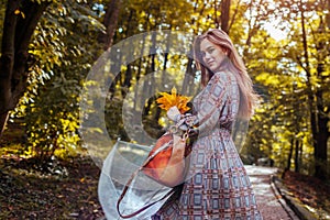 Happy young woman walking outdoors with transparent umbrella after rain holding leaves. Fall season activities