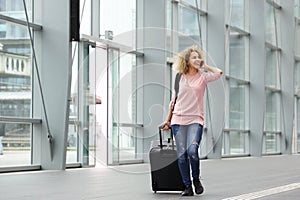 Happy young woman walking with suitcase and cell phone