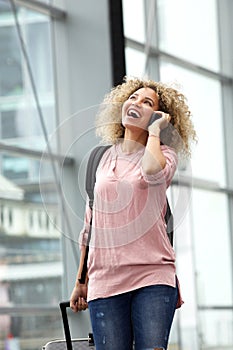 Happy young woman walking with suitcase and mobile phone