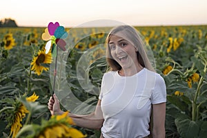 Happy young woman walking on sunflower field with windmill toy. Green energy concept
