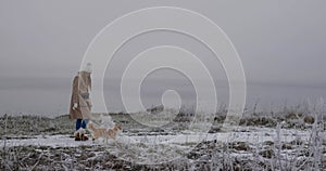 Happy young woman walking with welsh corgi pembroke puppy by winter sea