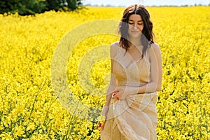 Happy young woman walking in yellow field on summer day. Pretty caucasian model girl with curly hair enjoying nature, dreaming,