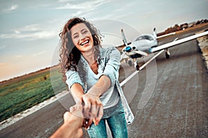 Happy young woman wants to fly in a small aircraft holding boyfriend`s hand