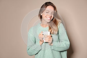 Happy young woman in warm sweater with cup of hot drink