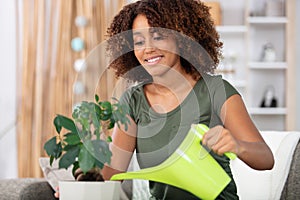 happy young woman watering houseplant