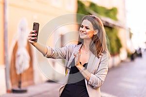 Happy young woman waving hand greeting during a phone video call in the street